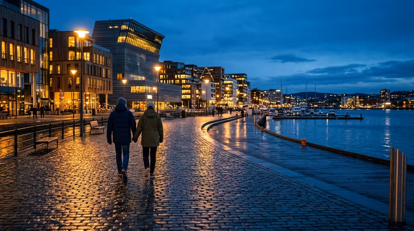 To personer går sammen langs en opplyst skandinavisk bryggepromenade i skumringen, trygge og offentlige omgivelser
